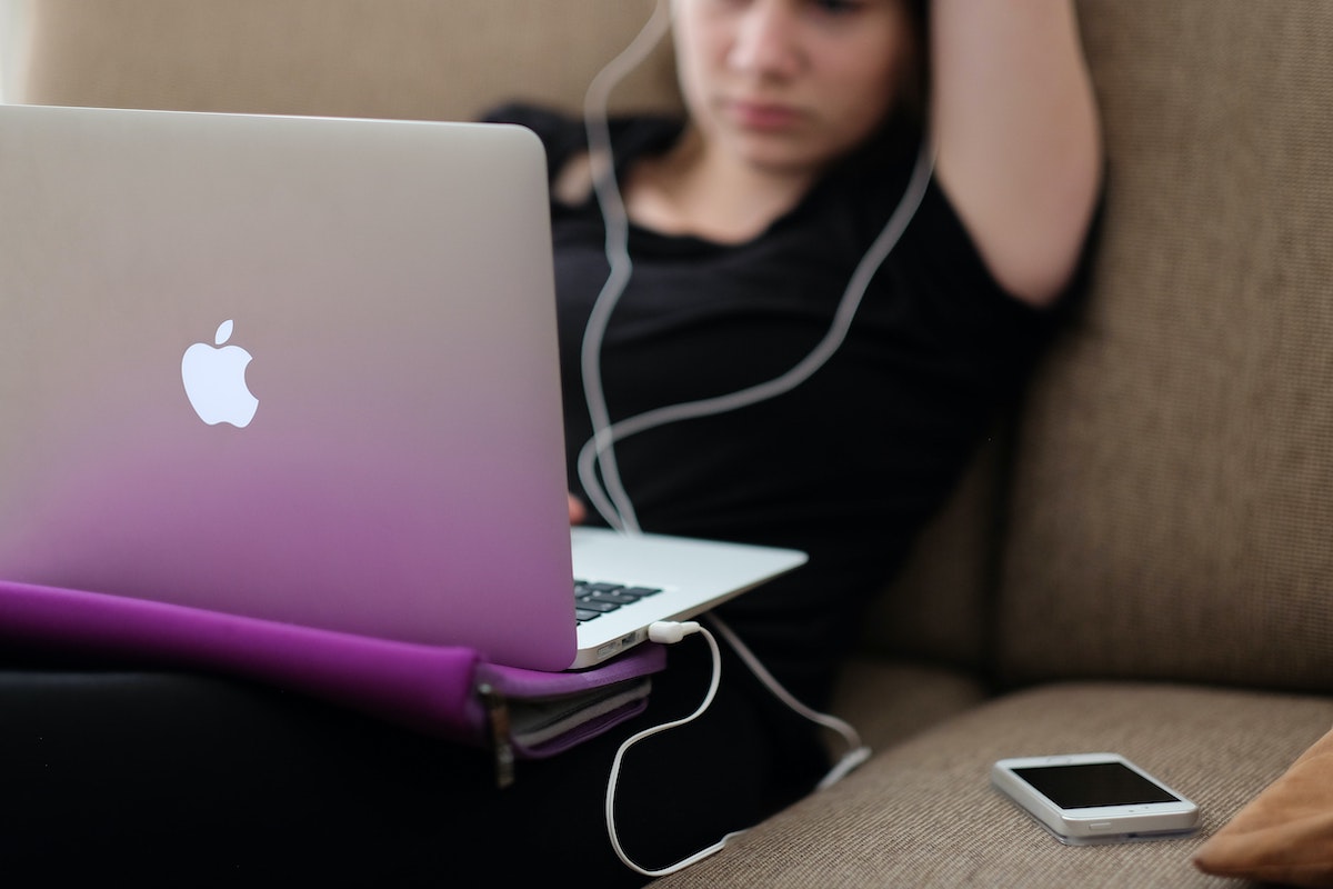 teenage girl sitting on couch looking at laptop with headphones in